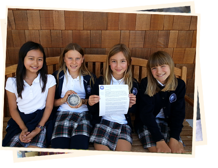 Four girls sitting on a bench holding papers.