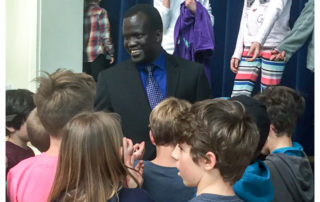A man in suit and tie standing next to a group of kids.