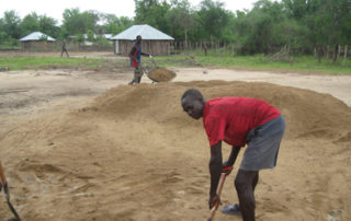 A man in red shirt and shorts digging hole.