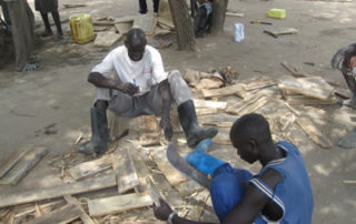 Two men sitting on the ground with a pile of wood.