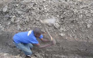 A man digging in the ground with an axe.
