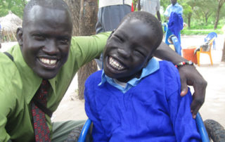Two men smile for a picture while sitting on the ground.