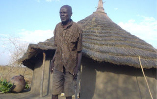 A man standing in front of a hut.