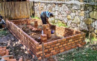 A person building a brick wall in the yard.